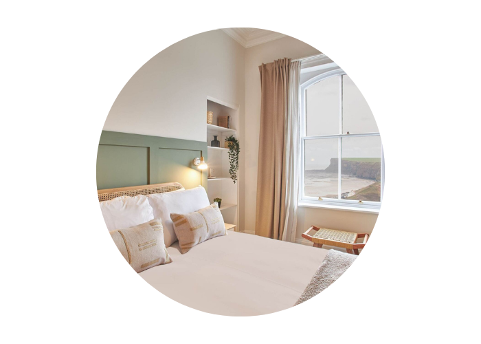 The bedroom in Huntcliff View in Saltburn-by-the-Sea, North Yorkshire. The image shows a bed in the forefront with a window showcasing amazing sea views in the background.