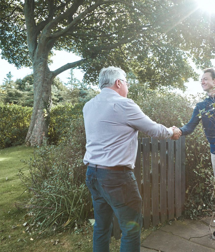 Two men shaking hands in a garden.