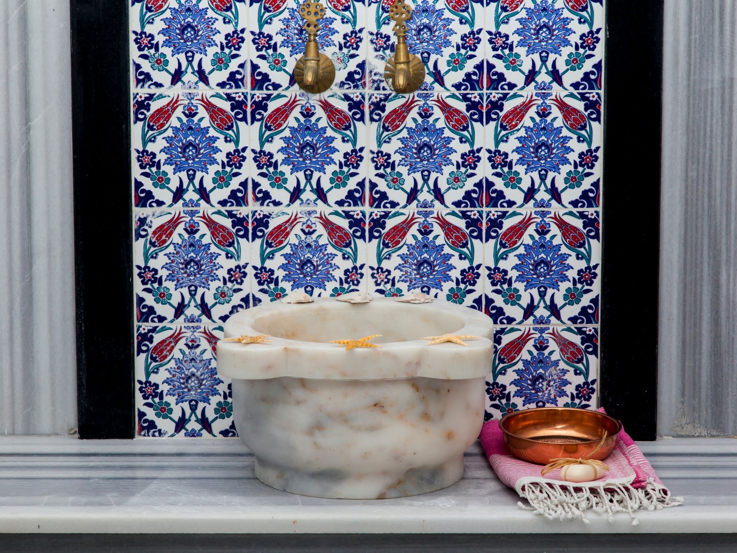 An image from the Turkish Baths showing beautiful, patterned wall tiles in blue, white and red, and an ornate sink. 