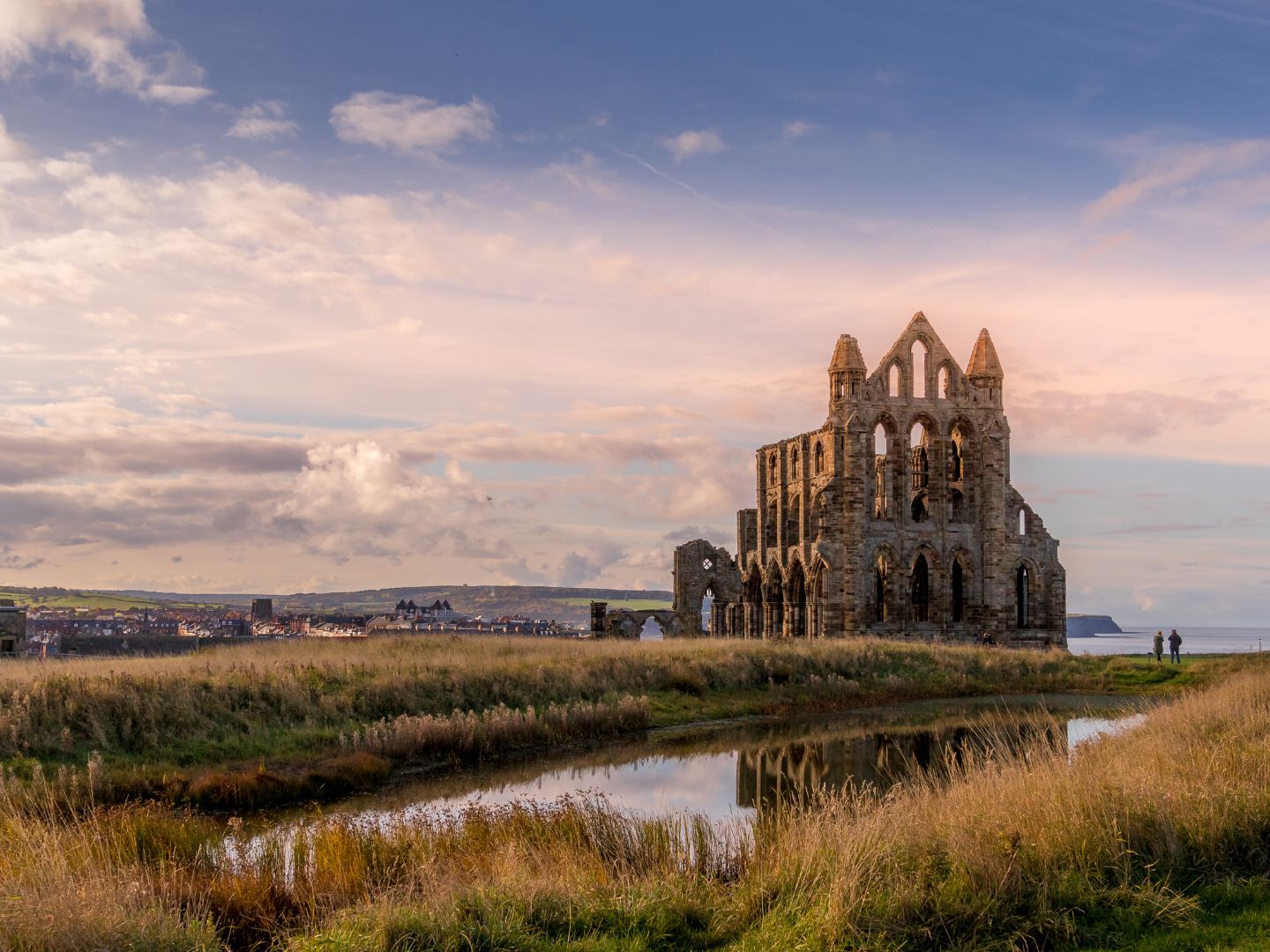 The image shows Whitby Abbey against a pink and blue sky.